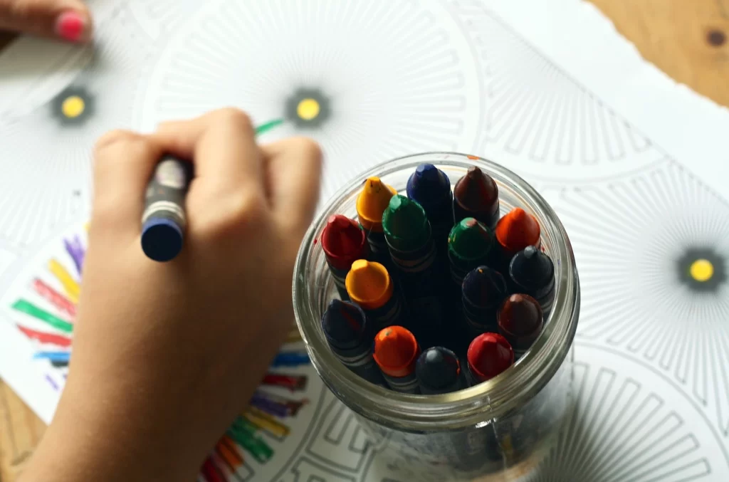 Copil ce desenează pe o foaie cu creioane cerate în culori diferite.